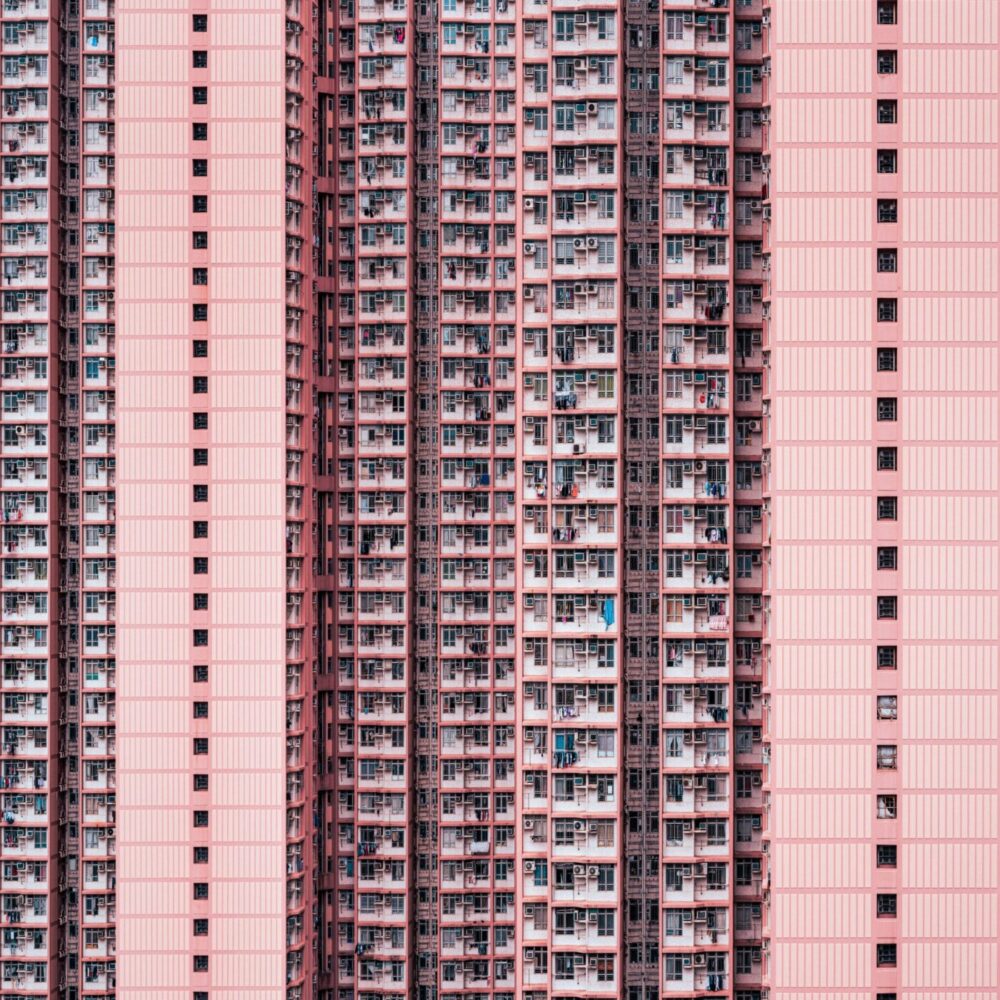 The tall residential building with a pink facade, named Density, features numerous balconies and uniform windows. Its repetitive architectural pattern evokes urban density and symmetry, reminiscent of an art prints meticulous design.