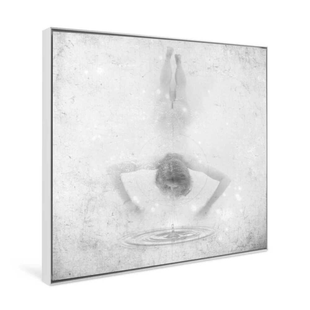 The black and white art print titled Ingrávido 008 depicts a person bending over a pool of water, their reflection creating ripples. Its textured, faded background enhances the dreamlike atmosphere. This captivating piece is elegantly framed on a square canvas.