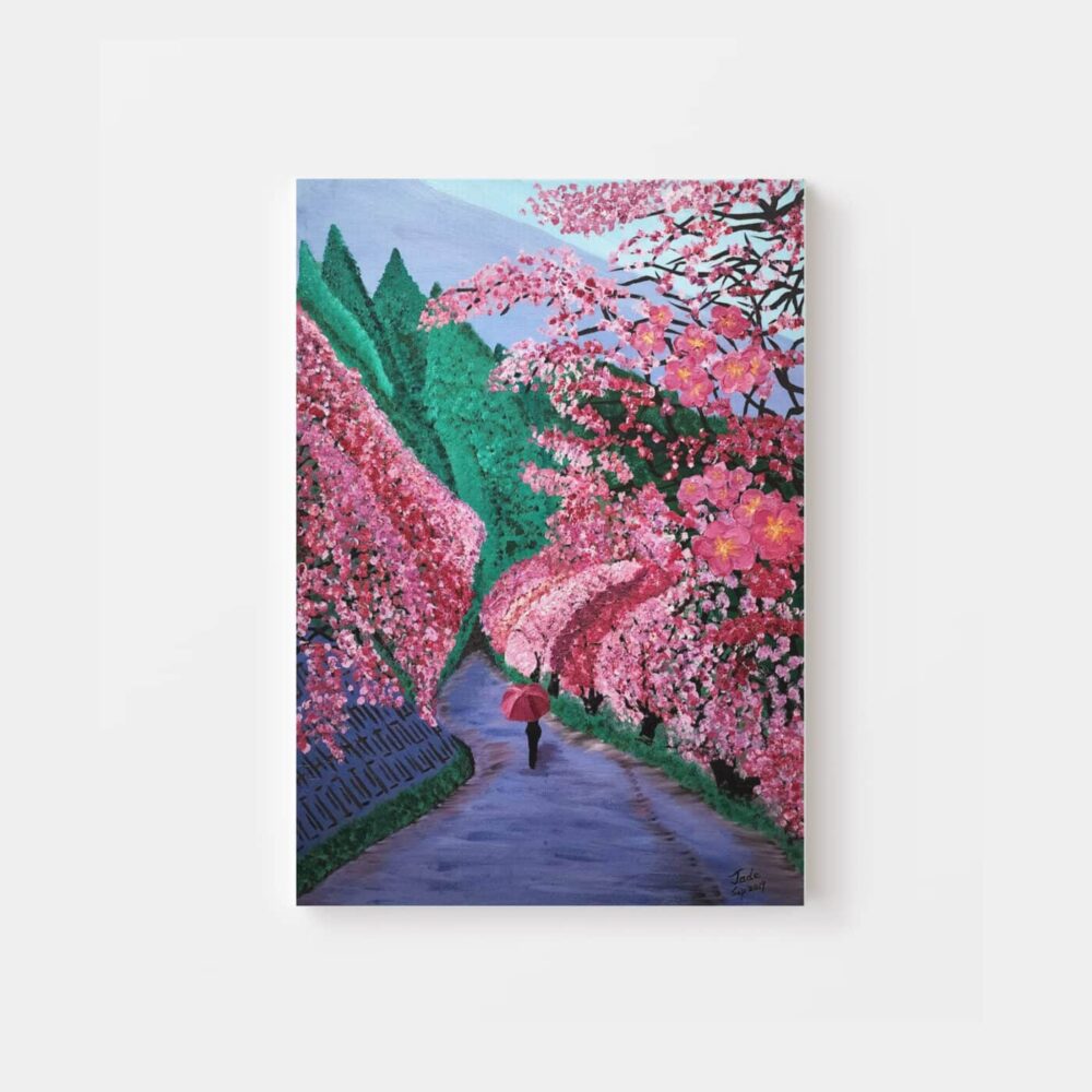 The Cherry Blossoms In The Valley art print captures a person with an umbrella walking along a cherry blossom-lined path. With vibrant pink blossoms and lush green trees, it evokes a serene springtime ambiance.