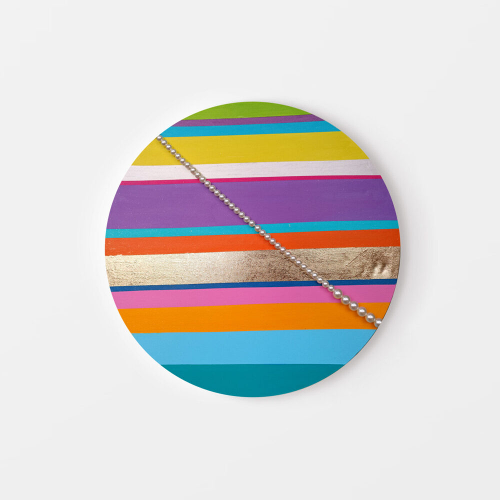 The Madam Saturne art print features an oval design with bold horizontal stripes in vibrant green, yellow, pink, purple, orange, and blue. A diagonal line of silver spheres adds texture and contrast against a white background.