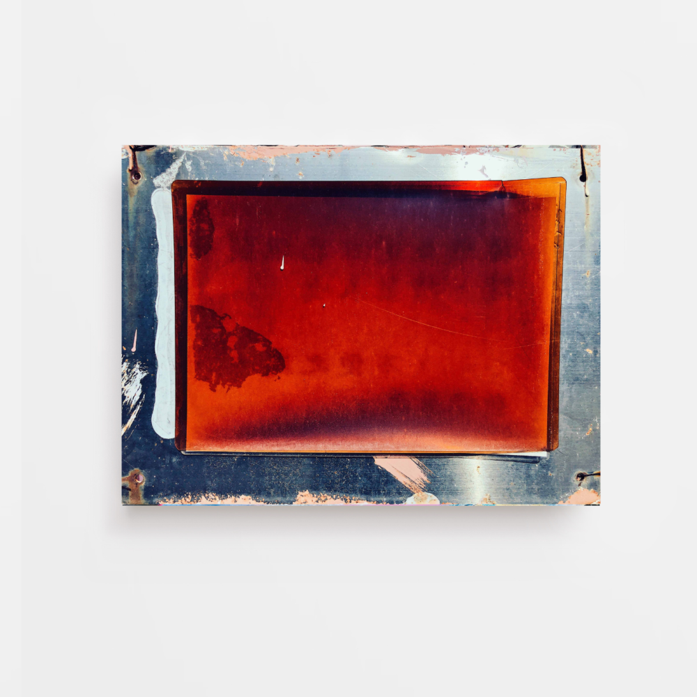 The Red Files is a rectangular metal frame with a transparent reddish-brown center, evoking an aged art print. It has visible scratches and wear, with the metal edges worn and slightly rusted, set against a plain white background.